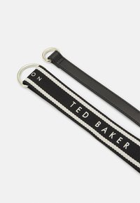 Zwarte stoffen band met witte touwachtige accenten en geborduurde tekst "TED BAKER," met metalen lussen aan beide uiteinden.