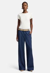Hvit kortermet t-skjorte kombinert med mørkeblå vide jeans i denim, med et beige belte og dekorative sko med gullaccenter.