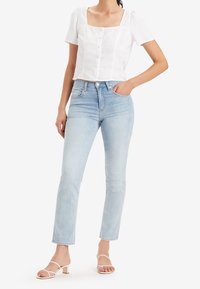 Blusa corta blanca de mangas cortas con escote cuadrado y cierre de botones, combinada con jeans de tiro alto en azul claro y sandalias con tiras.