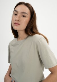 Helles graues Baumwoll-T-Shirt mit kurzen Ärmeln, einem Rundhalsausschnitt und einer glatten Textur. Keine auffälligen Muster oder Akzente sind sichtbar.