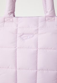 Ljust lila quiltad tote-väska med vadderade sektioner, med en texturerad yta och en subtil prägling av logotypen. Förstärkta handtag.