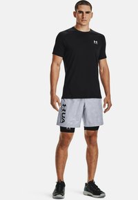 Camisa atlética negra de manga corta combinada con pantalones cortos grises de estampado camuflaje con acentos en negro y logo. Tejido ligero y transpirable.
