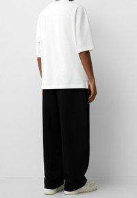 Hvid bomulds t-shirt med en afslappet pasform, korte ærmer og sømdetaljer. Kombineret med sorte bukser med vidde og lyse sneakers.