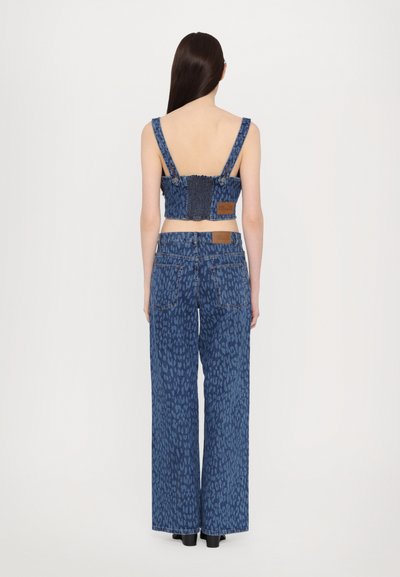 Δερμάτινη μπλούζα cropped με φαρδιές ράντες και σούρα στην πλάτη, σε συνδυασμό με ψηλόμεσα παντελόνια σε γραμμή φάρδους με μπλε λεοπάρ μοτίβο.