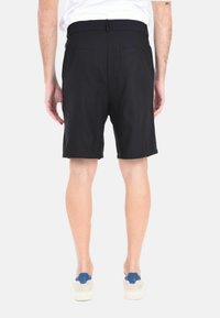 Pantaloni neri con vita media, dal texture morbido e dotati di due tasche posteriori. Abbinati a scarpe chiare.