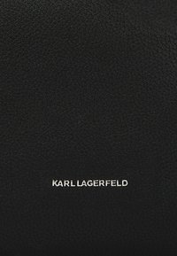 Črna usnjena tekstura z rahlo strukturo. Na dnu je srebrni logotip "KARL LAGERFELD". Minimalističen dizajn brez dodatnih akcentov.