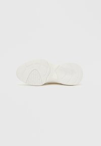 Weiße Sneaker-Außensohle mit strukturiertem Gummiprofil, das glatte und gemusterte Bereiche für Griffigkeit und Haltbarkeit aufweist. Leicht gebogenes Fußgewölbedesign.