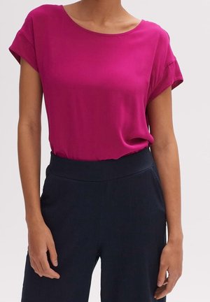 Fuchsia kurze Bluse mit rundem Ausschnitt aus glattem Stoff, kombiniert mit dunkelblauen Hosen mit strukturierter Oberfläche.