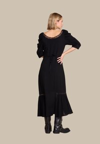 Svart kjole med puffermer, blonder detaljer ved utringningen og kanten, belte i midjen og utsvingt bunn. Parret med svarte knelang støvler.