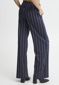 Marineblaue, weit geschnittene Hosen mit vertikalen goldenen Streifen, ausgestattet mit einem klassischen Bund, Gesäßtaschen und einer glatten, glänzenden Stoffoberfläche.