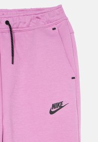 Ružové bavlnené tepláky s elastickým pásom, čiernym šnúrkou, bočnými vreckami a malým čiernym logom Nike na ľavom stehne.