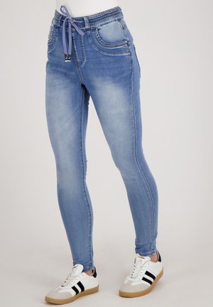 Lichtblauwe skinny jeans van denim met een elastische tailleband, trekkoorddetail en frontzakken, gecombineerd met witte sneakers en beige accenten.
