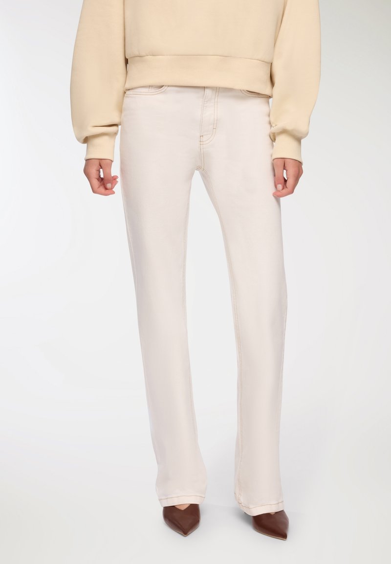 Jasnobeżowe, wysokie jeansy o prostym kroju nóg, z kontrastowymi szwami oraz gładką, lekko błyszczącą teksturą.