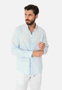 Camicia azzurra a maniche lunghe con colletto alla mandarina, chiusura con bottoni e dettagli dei polsini arrotolati, realizzata in un tessuto testurizzato.