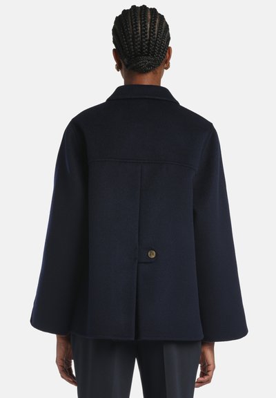 Tmavomodrý kabát z vlnenej zmesi s voľným strihom, širokými rukávmi, detailom s gombíkmi na zadnej strane a čistými líniami. Textúrovaná látka zvyšuje teplo.