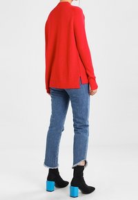 Red ribbed knit sweater with side slits, paired with light blue ankle-length jeans, and black ankle boots featuring blue block heels.