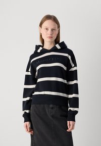 Felpa con cappuccio a righe blu navy e bianche, con un grande logo del marchio sul davanti, dotata di cappuccio con cordino e polsini a coste. Vestibilità casual.
