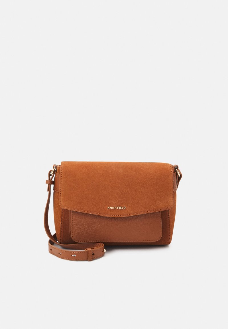 Brązowa zamszowa torebka typu crossbody z teksturowanym klapkiem, skórzanymi akcentami i regulowanym paskiem; posiada złote logo z przodu.