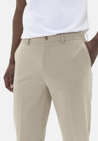Pantalon beige en tissu lisse, doté d'une fermeture à bouton et de poches latérales, avec une coupe ajustée et des détails de couture subtils.