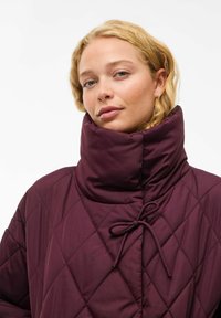 Quiltanaš burgundski sakou s visokim ovratnikom, s vezicom za zatvaranje, prikazuje glatku teksturu i uzorak dijamantnog dizajna.