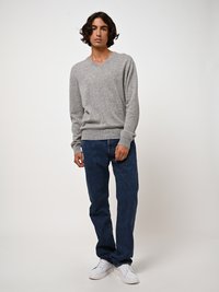 Grauer Strickpullover mit V-Ausschnitt, kombiniert mit dunkelblauen Jeans. Das Model trägt weiße Sneakers. Weicher Stoff, minimalistisches Design und klassischer Schnitt.