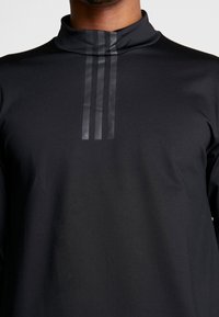 Schwarzes Langarmshirt mit hochgeschlossenem Kragen, versehen mit drei vertikalen grauen Streifen auf der Vorderseite. Hergestellt aus einem glatten, dehnbaren Material.