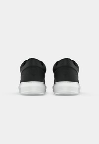 Adidași negri cu un superior neted, mat și o talpă din cauciuc alb. Au o formă rotunjită și un branding minim pe călcâi.