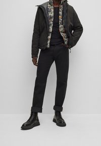 Chaqueta acolchada negra con un forro floral, camiseta negra de cuello redondo, pantalones negros remangados y botas negras con cordones. Look casual y en capas.