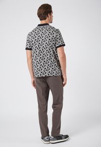 Kortärmad polo i svart och beige blommönster, matchad med grå rutiga byxor och grå skor med svarta accenter.