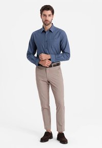 Camicia azzurra con bottoni e maniche lunghe, taschino sul petto, pantaloni beige su misura e scarpe marroni scure. Tessuto liscio con una vestibilità casual.