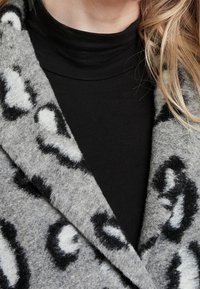 Grå ullrock med ett svart och vitt leopardmönster, med en djup V-ringad krage lager-på-lager över en svart långärmad topp.