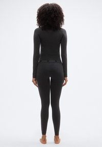 Γκρι εφαρμοστό τοπ με μακριά μανίκια και ταιριαστά κολάν από μαλακό, ελαστικό ύφασμα. Τα κολάν διαθέτουν ζώνη με σχέδιο και στενή εφαρμογή που αγκαλιάζει το σώμα.