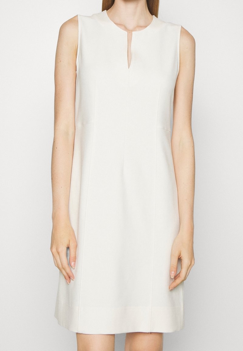 Robe beige sans manches avec un décolleté goutte d'eau, texture lisse, silhouette ajustée et détails de couture minimalistes sur l'ourlet.