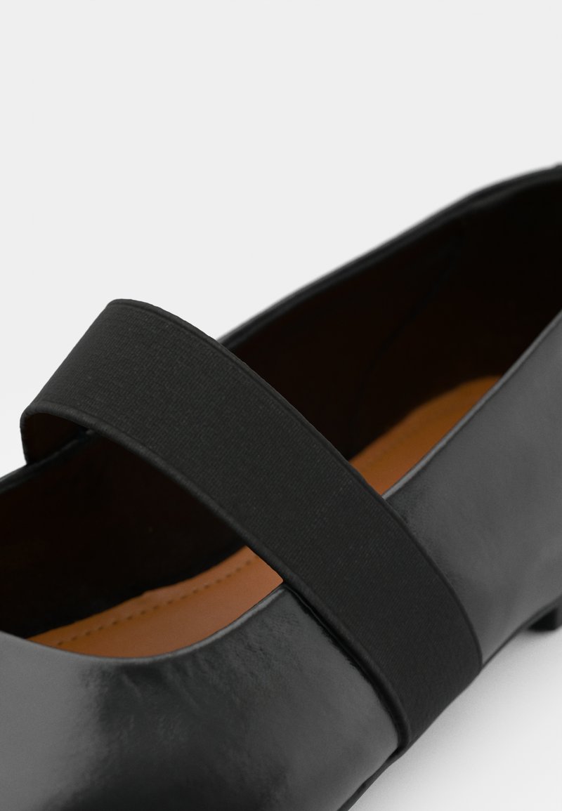 Chaussure en cuir noir avec une finition lisse, dotée d'une large sangle élastique noire et d'un doublure intérieure marron. Design à bout rond.
