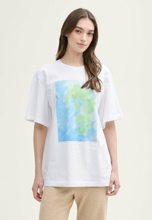 T-shirt blanc surdimensionné avec un imprimé abstrait bleu et vert sur le devant, fabriqué en coton, avec des manches courtes et un col rond.