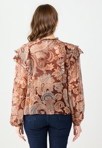 Brązowa bluzka we wzór kwiatowy z falbaniastymi rękawami i luźnym krojem. Wykonana z lekkiego materiału, ozdobiona skomplikowanymi wzorami paisley w beżu i niebieskim.