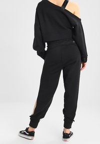 Svart croppad sweatshirt med off-shoulder-design, matchad med svarta joggers med sidsnitt. Används med svarta sneakers.