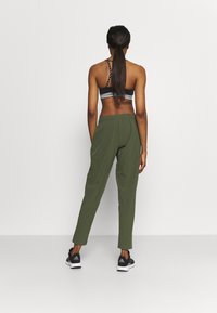Athletic outfit featuring a black sports bra with a crisscross back and green tapered pants. The pants have an elastic waistband and side pockets.