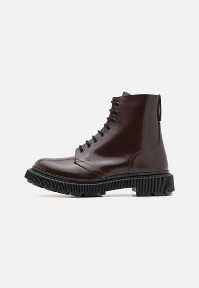 Des bottes de cheville en cuir marron avec une finition lisse, un bout rond, un laçage noir et une semelle en caoutchouc épaisse et crantée pour l'adhérence.