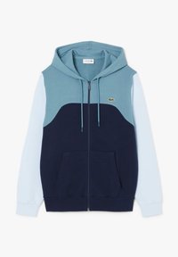 Kapturowana kurtka zapinana na zamek w kolorze niebieskim i granatowym, z panelem, kieszeniami kangurzymi oraz logo Lacoste na piersi. Wykonana z miękkiego materiału bawełnianego.
