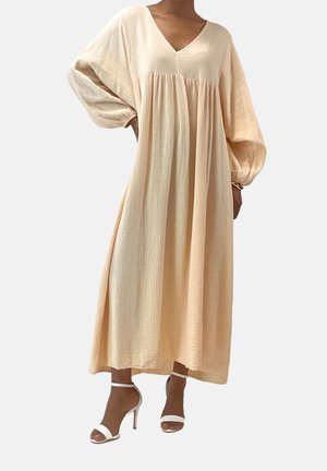 Lekka, różowawa sukienka maxi z dekoltem w serek, bufkami na rękawach i teksturowaną tkaniną. Połączona z białymi sandałami na obcasie.