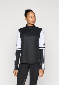 Zwarte sportieve pullover met een half-ritskraag, contrasterende witte mouwen en drie strepen op de armen; gemaakt van glad, lichtgewicht materiaal.