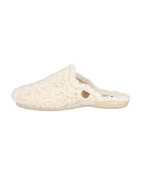 Zapatilla color crema con textura esponjosa, diseño tipo slip-on y punta redonda. Presenta un pequeño acento de logo circular en el lateral.