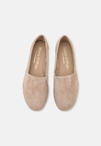 Chaussures slip-on beige en suede doux avec un bout arrondi et des détails cousus autour des bords. La doublure intérieure est de couleur brun clair.
