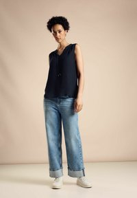 Top senza maniche blu marino con scollo a V e cordoncino regolabile, abbinato a jeans a gamba larga azzurri e sneakers bianche. Outfit semplice e casual.