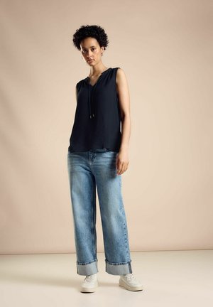 Top senza maniche blu marino con scollo a V e cordoncino regolabile, abbinato a jeans a gamba larga azzurri e sneakers bianche. Outfit semplice e casual.