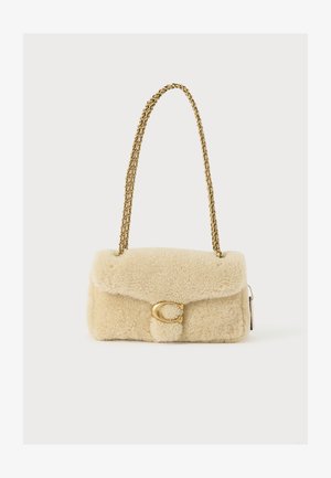 Bézs birkabőr válltáska aranylánc pánttal és arany csattal, amely C betű alakú a táska elülső fedelén.