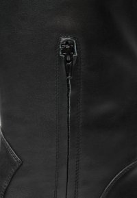 Černá kožená bota s bočním zipem, hladkým povrchem a minimalistickým designem se švy a zakřivenou panelou.