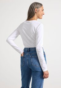 Vit långärmad topp i kombination med högmidjade blå denimjeans. Toppens halsringning är rundad och ärmarna är figursydda. Jeansen har bakfickor.