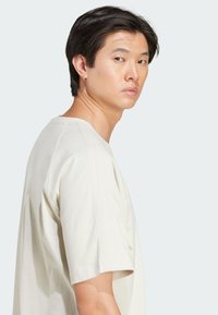 Chemise en coton beige clair à manches courtes avec des accents côtelés sur les épaules et une coupe décontractée. Texture douce, col rond, design minimaliste.